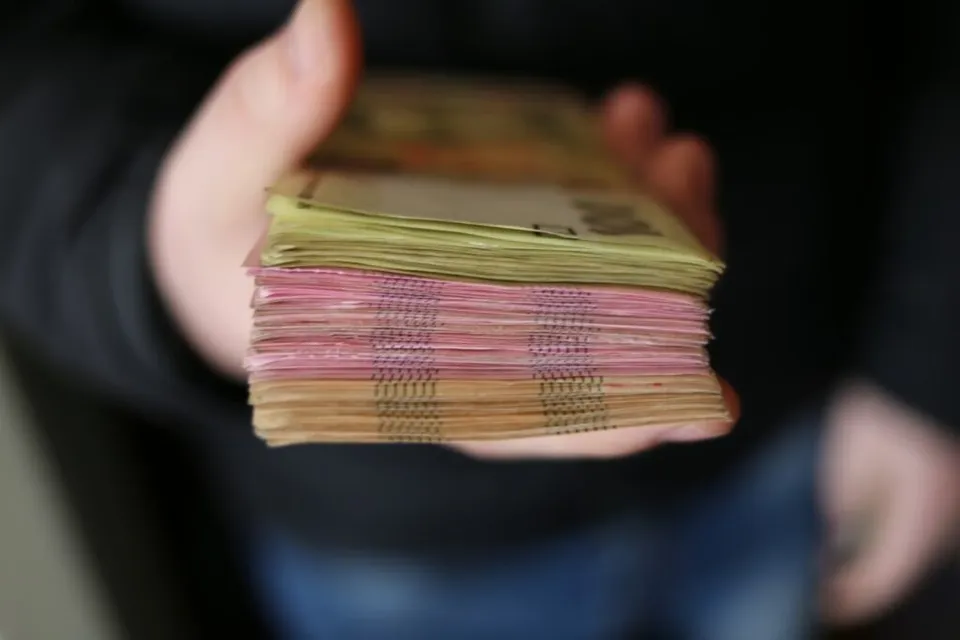O persoană ține în palmă un teanc gros de bancnote colorate.