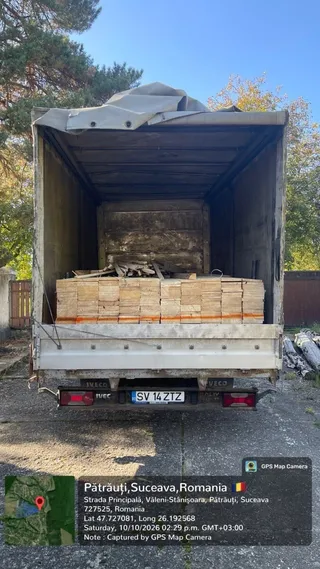 O autoutilitară albă cu spatele deschis este încărcată cu plăci de cherestea depozitate în interiorul compartimentului de marfă.