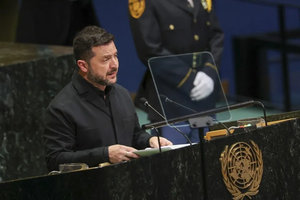 Un bărbat cu barbă și păr scurt, îmbrăcat în haine negre, stă în spatele unui pupitru cu emblema ONU și vorbește.