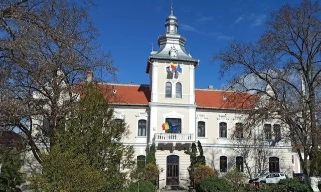 O clădire cu acoperiș roșu și un turn central sub un cer albastru, înconjurată de copaci fără frunze.
