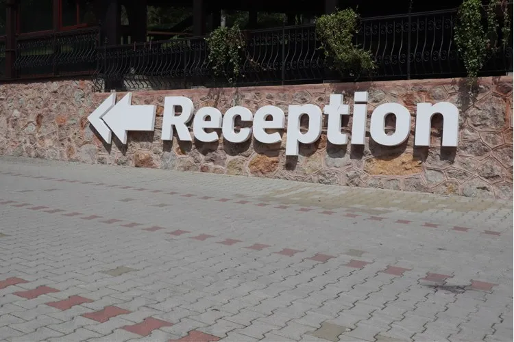 Un semn alb cu textul Reception și o săge pointing spre stânga este montat pe un perete de piatră.