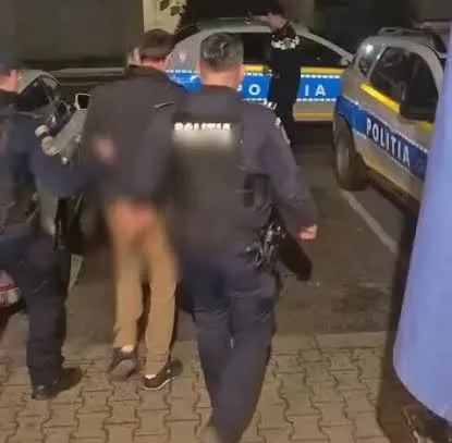 Unii polițiști în uniformă stau lângă mașini de serviciu marcate cu inscripția Politia pe un drum pavat noaptea.
