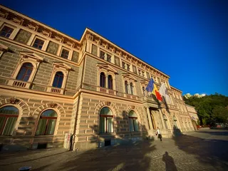 O clădire înaltă cu ferestre mari și arcade este situată sub un cer albastru, având câteva steaguri suspendate pe fațadă.