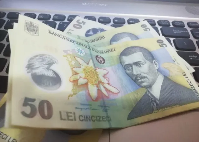 Bancnote de 50 de lei românești așezate pe o tastatură de laptop, cu portretul lui Nicolae Milescu și floarea de colt.
