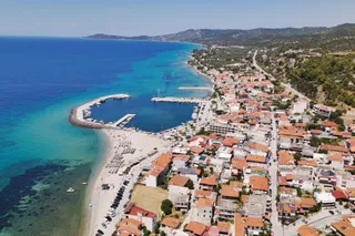 O vedere aeriană a unui oraș de coastă cu case cu acoperișuri roșii, o plajă nisipoasă și un port situat lângă o mare de culoare turcoaz.