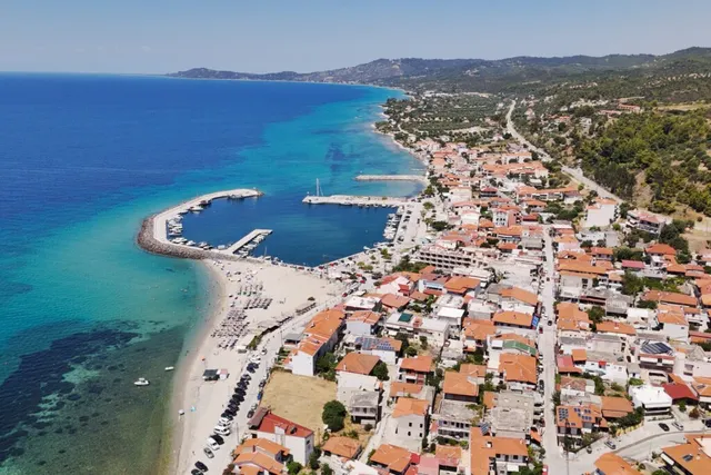 O vedere aeriană a unui oraș de coastă cu case cu acoperișuri roșii, o plajă nisipoasă și un port situat lângă o mare de culoare turcoaz.