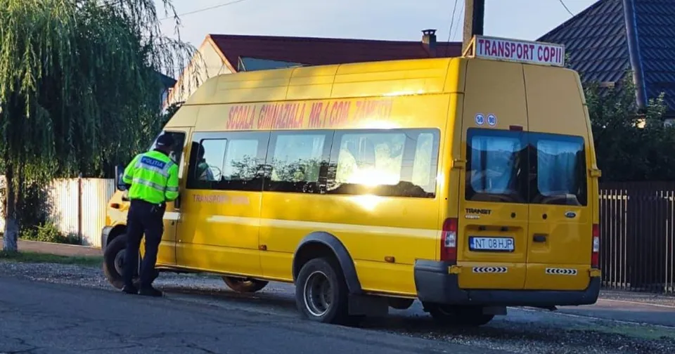 Un agent de poliție în uniformă fluorescente verifică un microbuz galben parcat pe marginea unui drum lângă un copac.