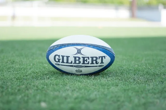 Un rugină de rugby albă cu detalii albastre este așezată pe un teren de iarbă verde.