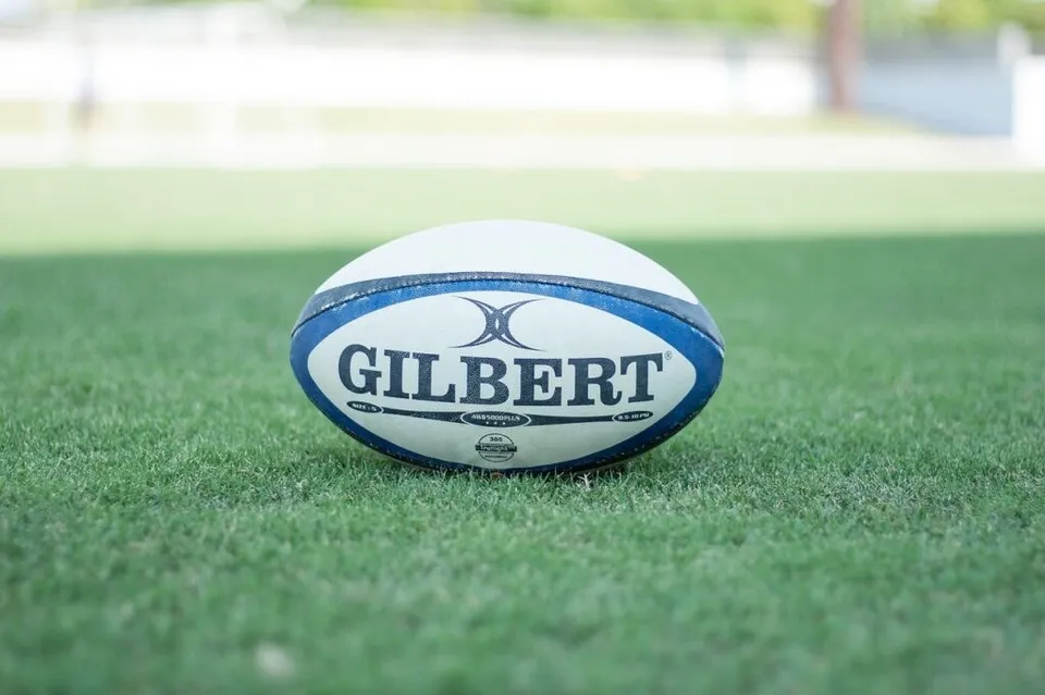 Un rugină de rugby albă cu detalii albastre este așezată pe un teren de iarbă verde.