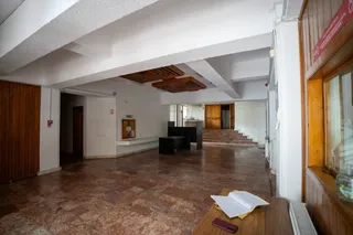 Un spațiu interior cu podea de piatră, pereți albi, grinzi de susținere albe și un mobilier negru situat în fundal.