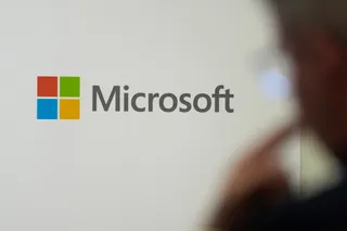 Logo-ul Microsoft pe un fundal alb, cu o persoană neclară în prim-plan, în dreapta.