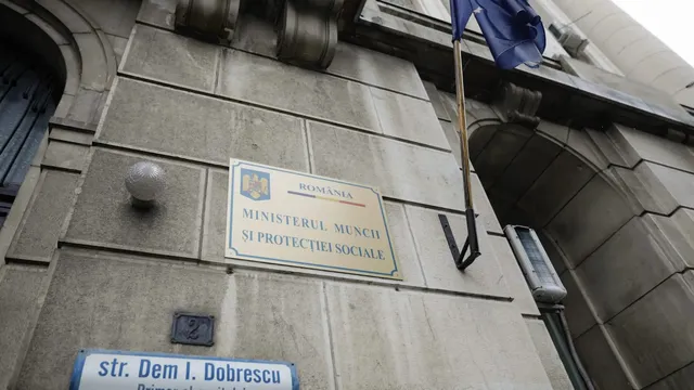 O placă cu textul Ministerul Muncii și Protecției Sociale este montată pe un perete de piatră al unei clădiri lângă un stâlp de iluminat.