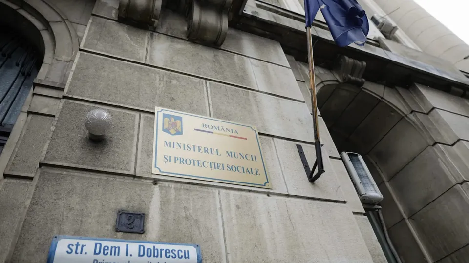 O placă cu textul Ministerul Muncii și Protecției Sociale este montată pe un perete de piatră al unei clădiri lângă un stâlp de iluminat.