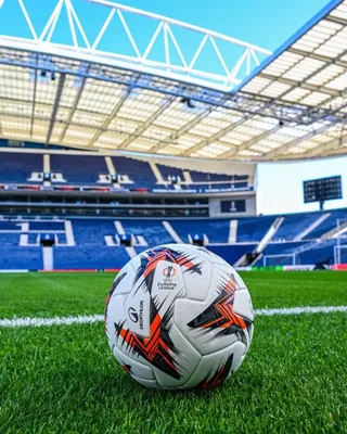 Un fotbal alb cu modele geometrice negre și roșii este plasat pe un teren de gazon verde cu o linie albă.