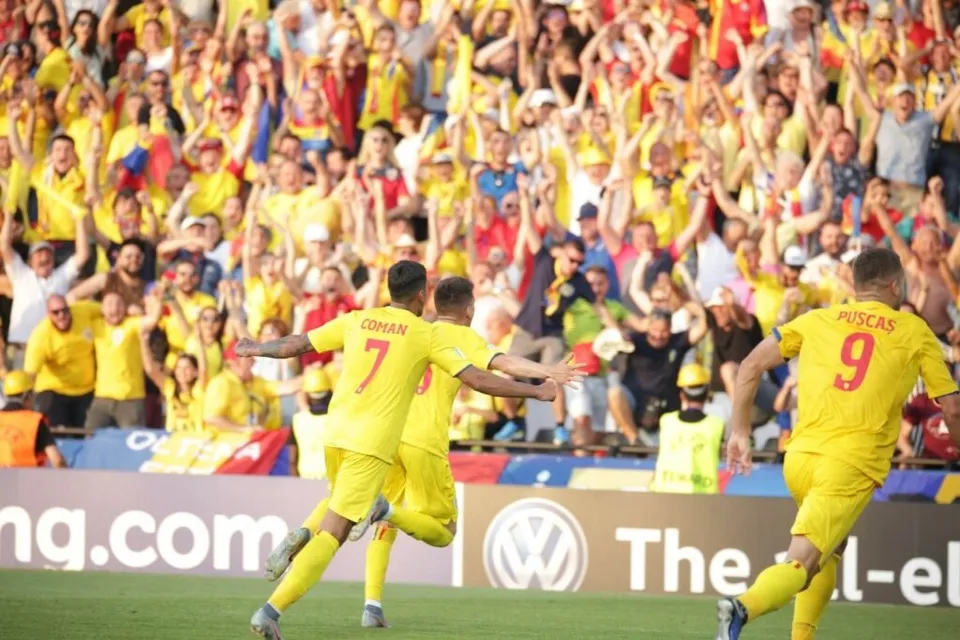 Câțiva jucători de fotbal în echipamente galbene celebrează pe un teren verde în fața unei mulțimi de spectatori care poartă haine galbene și roșii.