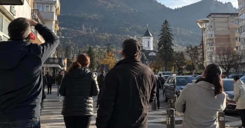 Cinci persoane stau cu spatele, privind spre un deal împădurit cu clădiri și un turn alb sub un cer senin.