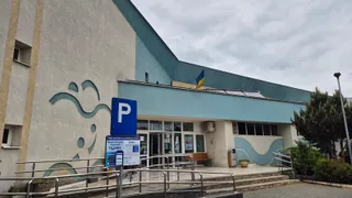 O clădire cu fațadă gri și albastră prezintă un semn de parcare albastru și o rampă metalică în prim-plan.