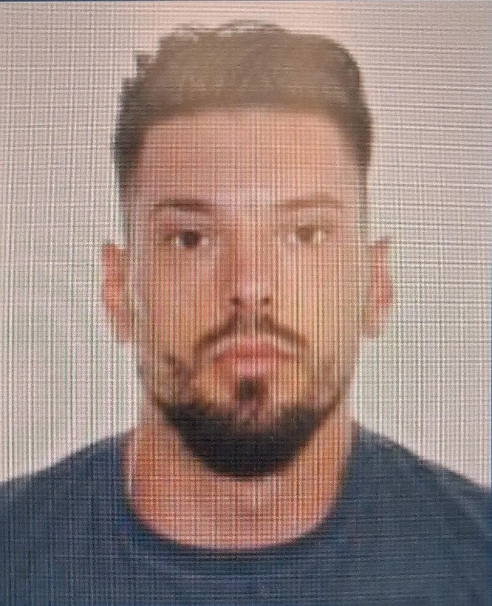 Un bărbat cu părul scurt și barbă neagră poartă un tricou albastru în fața unui fundal neutru.