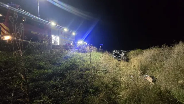 Un autoturism răsturnat se află în iarbă, lângă un vehicul de serviciu cu lumini aprinse, sub un cer de noapte întunecat.