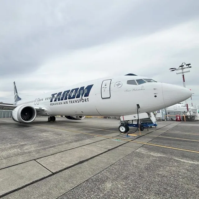 Un avion alb cu inscripția TAROM este parcat pe o pistă de beton sub un cer înnorat.