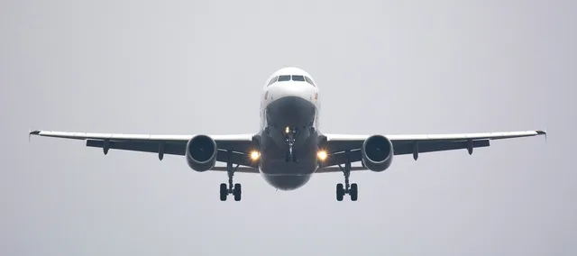 Un avion de pasageri alb cu două motoare și tren de aterizare extins zboară pe un cer gri.