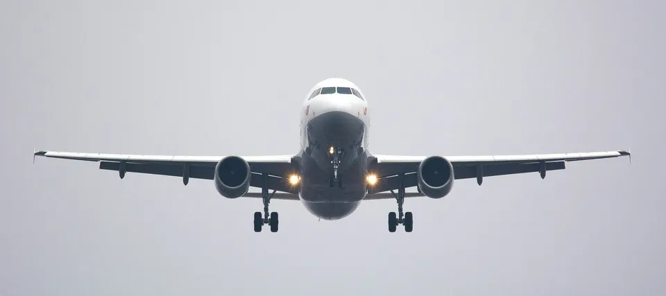 Un avion de pasageri alb cu două motoare și tren de aterizare extins zboară pe un cer gri.