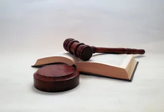 Un ciocan de lemn și o bază circulară sunt așezate deasupra unei cărți deschise pe un fundal alb.