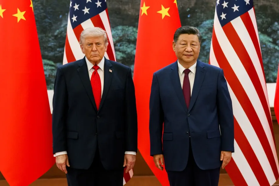 Doi bărbați în costume oficiale stau în picioare în fața unor steaguri americane și chinezești.