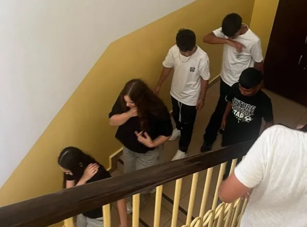 Mai mulți copii coboară pe o scară interioară lângă un balustrad de lemn și metal.