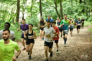 Un grup de oameni în echipamente sportive aleargă pe un drum de pământ într-o zonă împădurită.