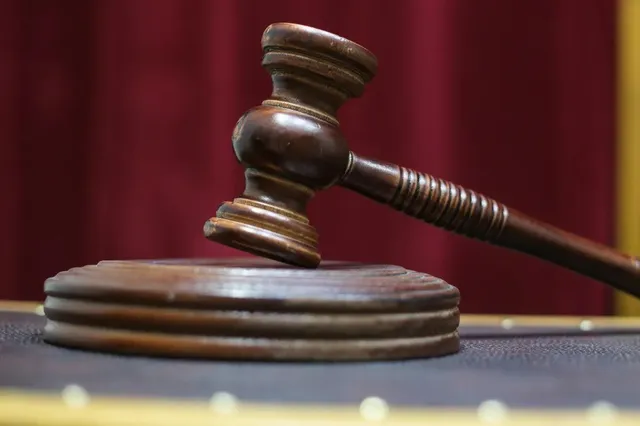 Un ciocan de lemn pentru judecătoră este așezat pe o bază circulară de lemn în fața unui fundal roșu.