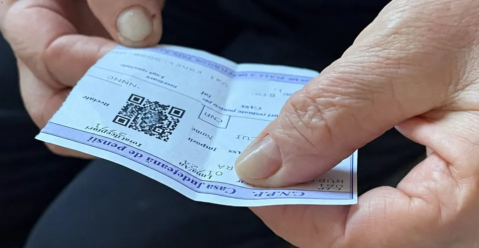 Mâinile unei persoane țin un talon de pensie alb cu text și un cod QR imprimat pe suprafața acestuia.