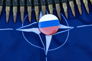 Mai multe gloanțe sunt așezate în arc deasupra unui steag albastru cu un simbol alb, având un buton rotund cu culorile tricolorului rus în centru.