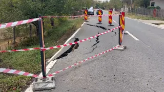 O porțiune de asfalt este ruptă și delimitată de benzi de semnalizare alb-roșii și conuri de trafic pe un drum asfaltat.