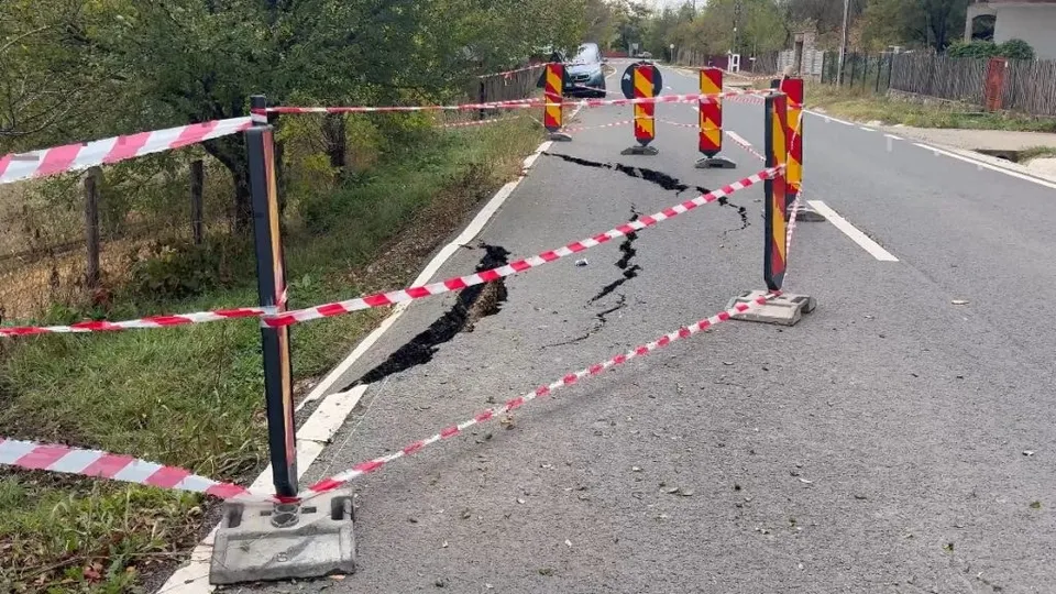 O porțiune de asfalt este ruptă și delimitată de benzi de semnalizare alb-roșii și conuri de trafic pe un drum asfaltat.