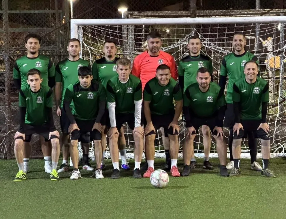 O echipă de minifotbal îmbrăcată în verți și negru, cu un portar în roșu, pozată pentru o poză de grup în fața unei porți.