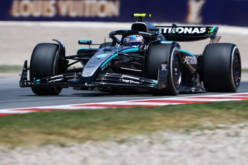 Un monopost de Formula 1 de culoare neagră și turcoaz circulă pe o pistă de curse cu borduri roșii și albe.