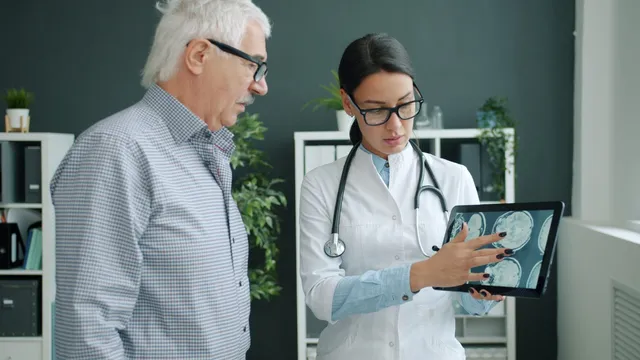 O femeie cu halat alb și stetoscop arată unui bărbat cu ochelari imagini medicale afișate pe o tabletă digitală.