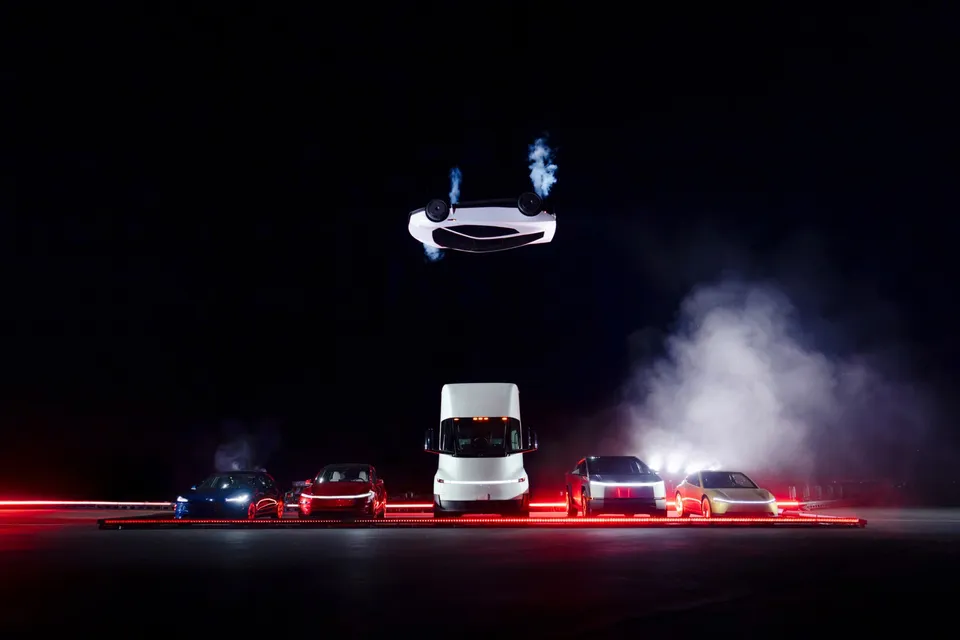 Un autoturism alb este suspendat în aer, cu flăcări albastre ieșind de sub roți, deasupra unui rând de mașini parcate pe un fundal întunecat.
