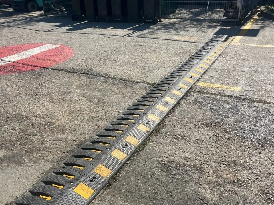 Un dispozitiv de tip bumper, de culoare neagră cu marcaje galbene, este montat pe o suprafață asfaltată lângă o zonă marcată cu vopsea roșie și albă.