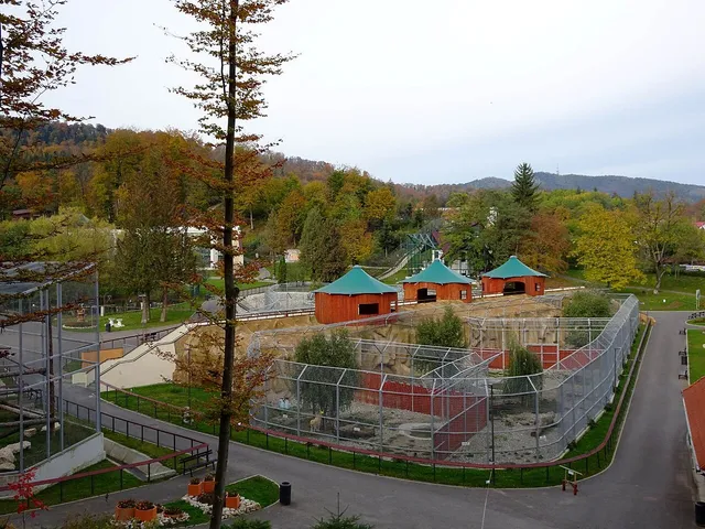 Vederea de sus prezintă diverse cuști de animale cu garduri metalice și structuri acoperite în mijlocul unui peisaj cu copaci și dealuri împădurite.