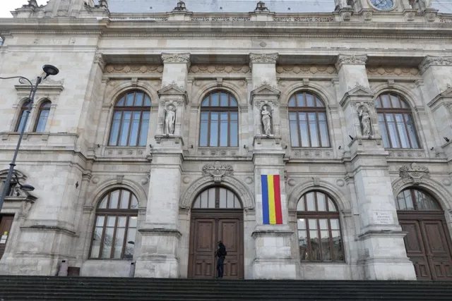O persoană stă în fața unei uși de lemn de la o clădire monumentală cu ferestre arcuite și statui în nișe.