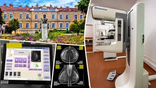 Un dispozitiv medical alb de mamografie stă într-o cameră, lângă un monitor care afișează imagini medicale și un ecran cu radiografii mamare.