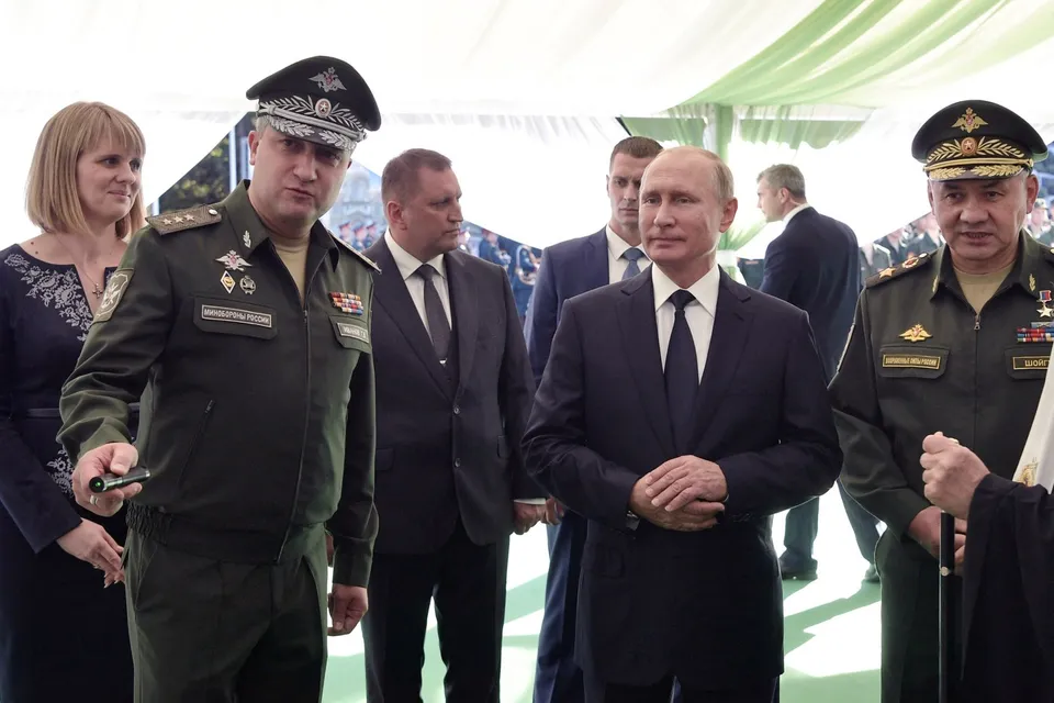 Un grup de bărbați în costume și uniforme militare stau în picioare sub o cortină de culoare deschisă.