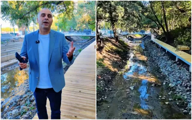 Un bărbat într-un sacou albastru și tricou alb stă pe o cărare de lemn lângă un șanț cu apă și pietriș.