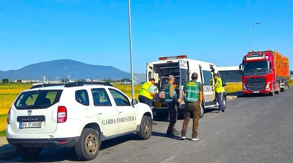 Un vehicul alb de serviciu este parcat pe un drum lângă un van alb, în timp ce patru persoane în veste reflectorizante stau lângă vehicule.