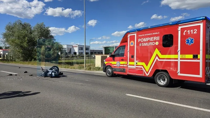 Un vehicul de intervenție roșu și galben este parcat pe marginea unei drumuri asfaltate lângă un obiect întunecat și deformat.