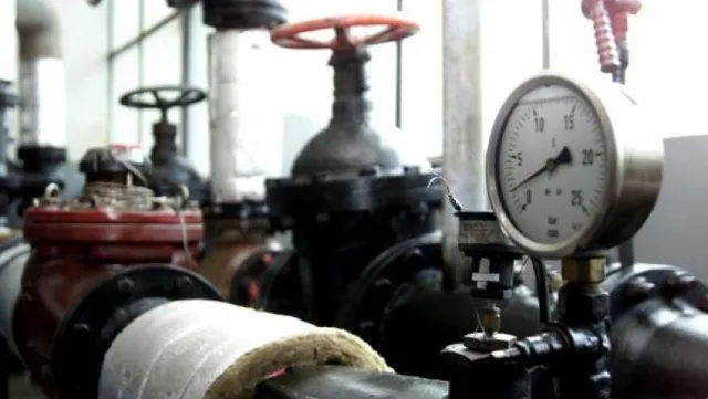 Un manometru cu cadran alb afișează valori numerice, fiind montat pe o conductă metalică lângă o supapă cu roată roșie într-o instalație industrială.