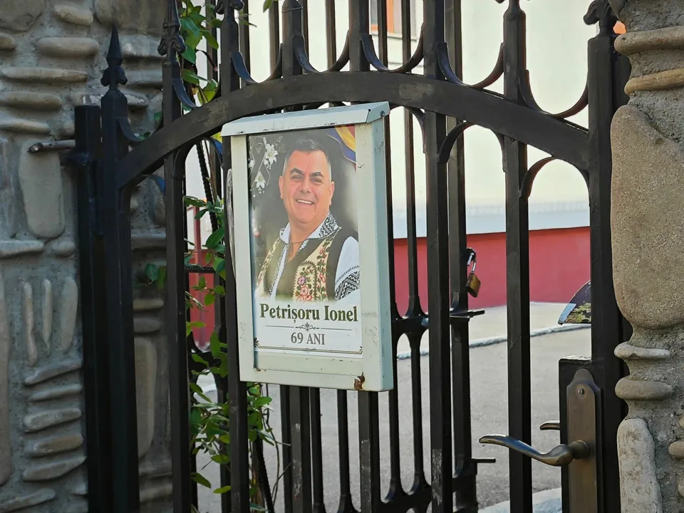 Un cadru cu un portret încadrat într-o cutie albă, afișat pe o poartă metalică neagră.