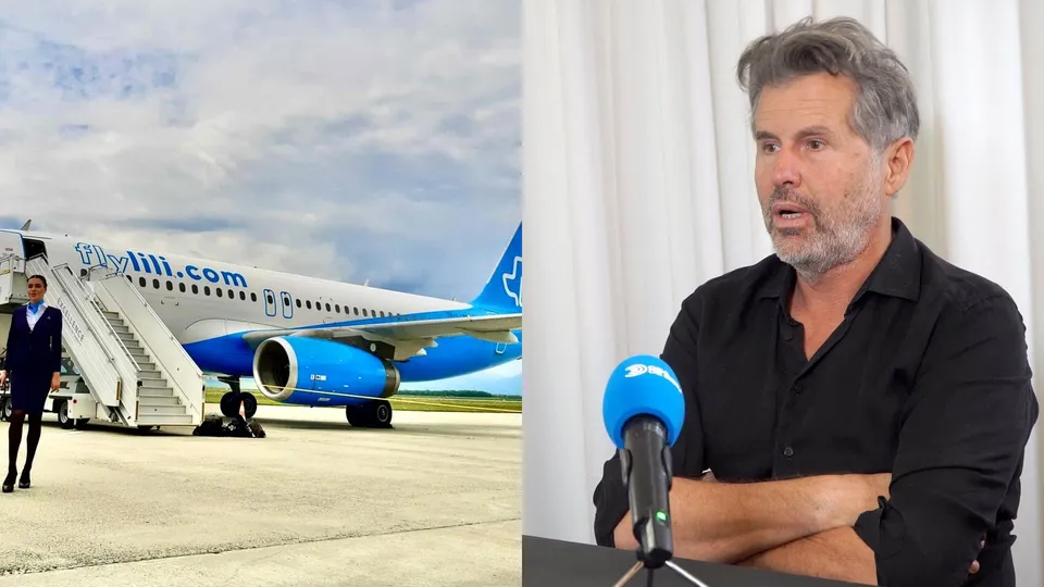 Un avion alb cu detalii albastre stă pe pistă lângă o scară mobilă, în timp ce un bărbat în costum negru stă lângă ea.